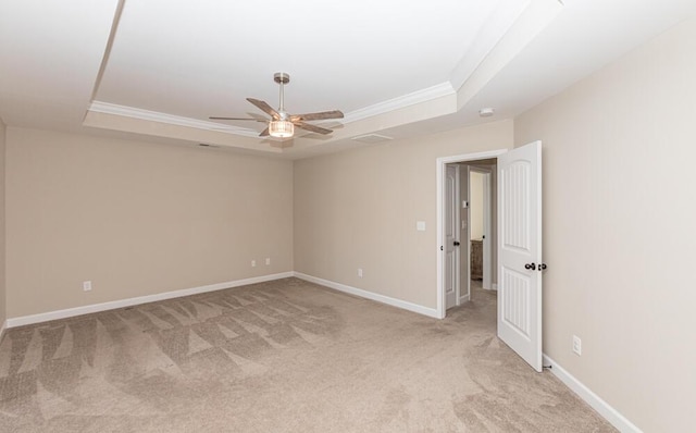 empty room with baseboards, a tray ceiling, and light colored carpet