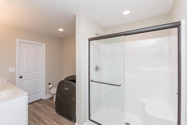 bathroom with recessed lighting, toilet, a stall shower, vanity, and wood finished floors