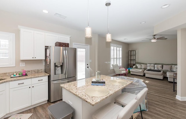 kitchen featuring white cabinets, a kitchen island, a breakfast bar, wood finished floors, and stainless steel refrigerator with ice dispenser