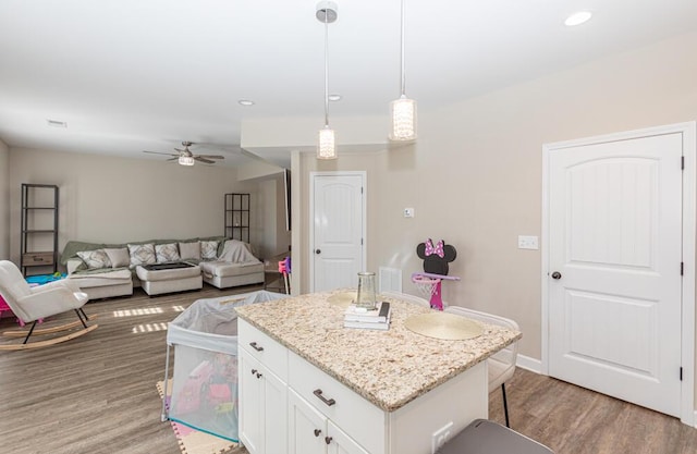 kitchen with light stone counters, a center island, hanging light fixtures, light wood-type flooring, and white cabinetry