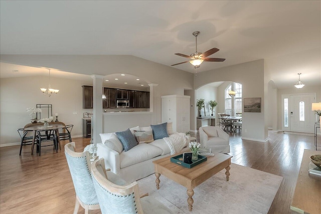 living room with arched walkways, light wood-style flooring, ceiling fan with notable chandelier, baseboards, and vaulted ceiling