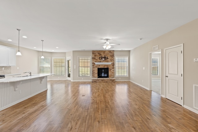 unfurnished living room with ceiling fan, a stone fireplace, visible vents, a healthy amount of sunlight, and light wood-style floors