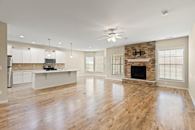 unfurnished living room with ceiling fan, a fireplace, light wood-style flooring, and baseboards