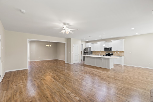 unfurnished living room with light wood-style floors, recessed lighting, baseboards, and ceiling fan with notable chandelier