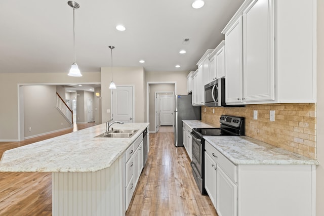 kitchen with tasteful backsplash, an island with sink, stainless steel appliances, light wood-type flooring, and a sink