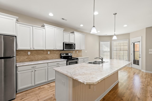 kitchen featuring a sink, appliances with stainless steel finishes, backsplash, light wood finished floors, and a center island with sink