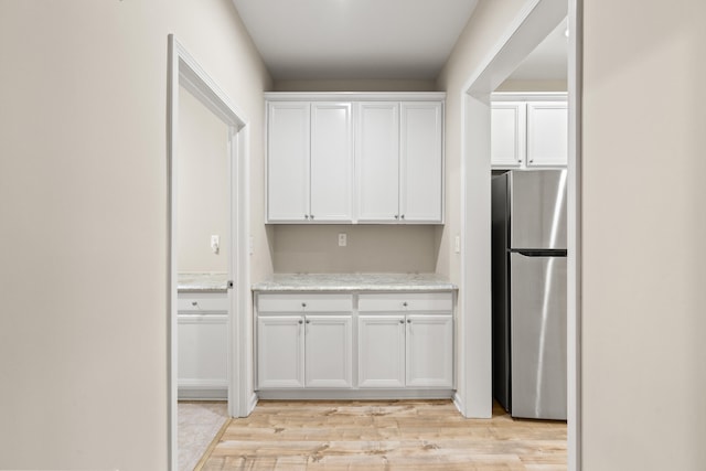 kitchen with light wood-type flooring, freestanding refrigerator, white cabinetry, and light stone countertops