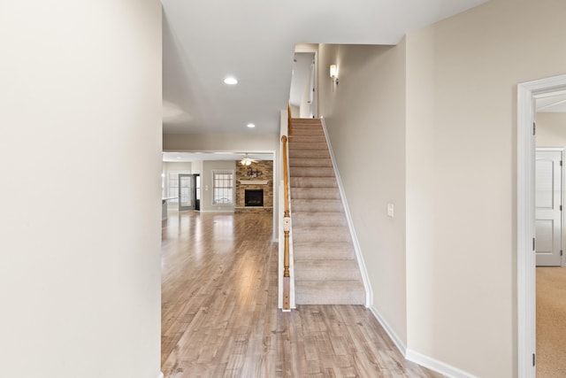 stairs featuring a fireplace, baseboards, wood finished floors, and recessed lighting