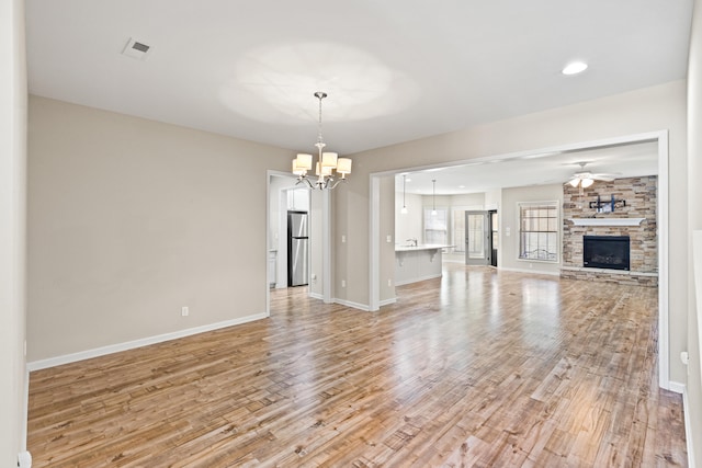 unfurnished living room with baseboards, a stone fireplace, light wood finished floors, and ceiling fan with notable chandelier