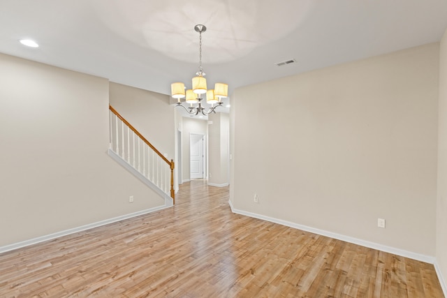 spare room featuring light wood-style floors, a notable chandelier, baseboards, and stairs