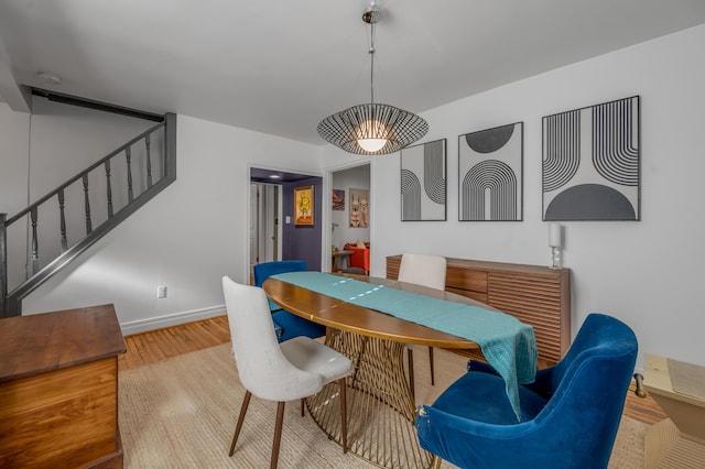 dining space with light wood finished floors, baseboards, and stairway