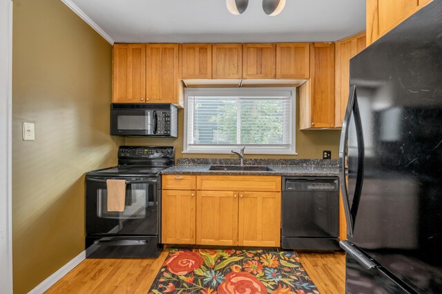 kitchen with black appliances, light wood-type flooring, dark countertops, and a sink