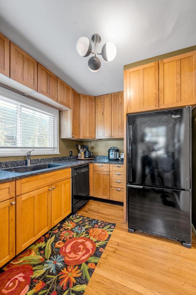 kitchen with dark countertops, light wood-style floors, brown cabinetry, a sink, and black appliances