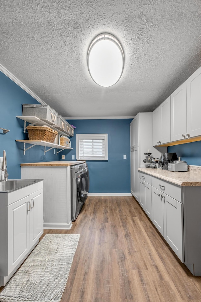 clothes washing area featuring ornamental molding, washer / dryer, cabinet space, and light wood-style flooring