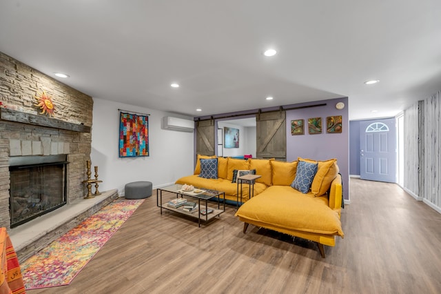 living room featuring a fireplace, recessed lighting, a barn door, wood finished floors, and a wall mounted air conditioner