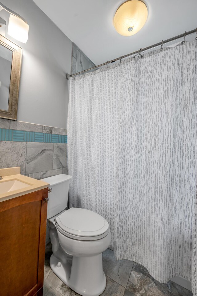 full bath featuring toilet, a wainscoted wall, a shower with shower curtain, vanity, and tile walls