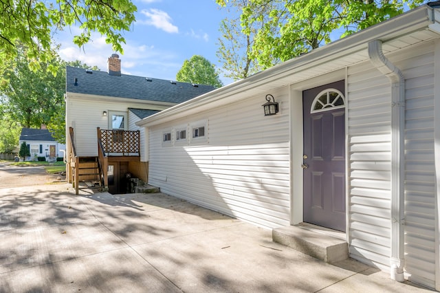 doorway to property featuring roof with shingles, a chimney, and a patio area