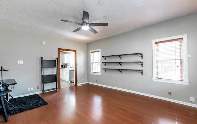 interior space featuring a ceiling fan, baseboards, dark wood finished floors, and a textured ceiling