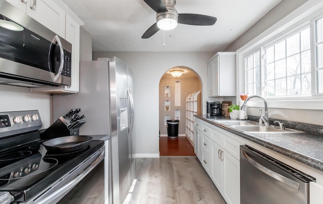 kitchen with appliances with stainless steel finishes, arched walkways, white cabinetry, and a sink