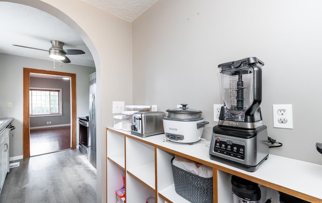 kitchen with arched walkways, a ceiling fan, wood finished floors, stainless steel appliances, and light countertops