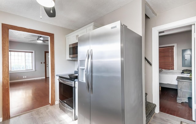 kitchen with light wood-style floors, appliances with stainless steel finishes, white cabinets, and a textured ceiling