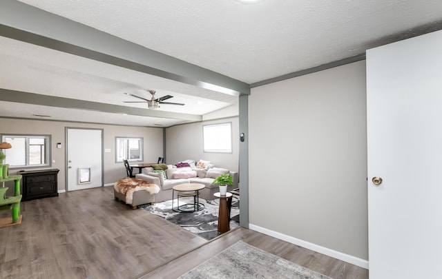 living area with ceiling fan, a textured ceiling, baseboards, and wood finished floors