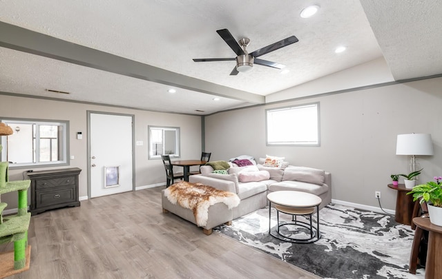 living room featuring a textured ceiling, beamed ceiling, baseboards, and light wood-style floors