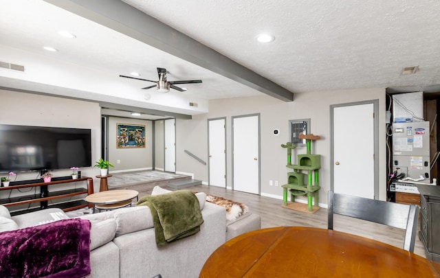 living area with a textured ceiling, wood finished floors, visible vents, a ceiling fan, and beam ceiling