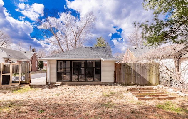 rear view of property featuring a shingled roof, a gate, a sunroom, and fence