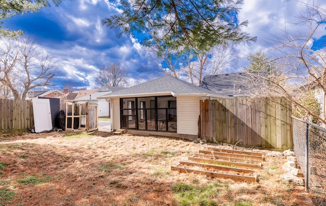 rear view of property featuring an outbuilding, roof with shingles, a sunroom, a shed, and a fenced backyard