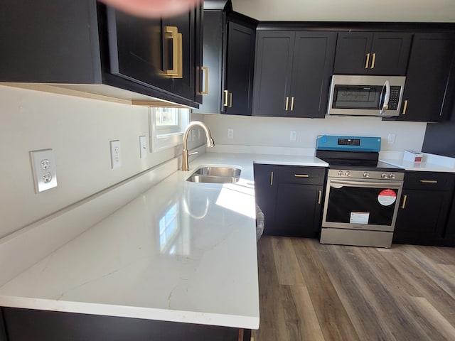 kitchen featuring wood finished floors, a sink, appliances with stainless steel finishes, dark cabinetry, and light stone countertops