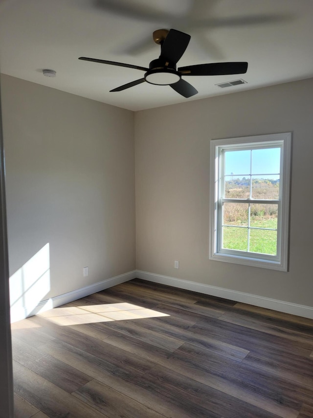 spare room with dark wood-type flooring, visible vents, ceiling fan, and baseboards