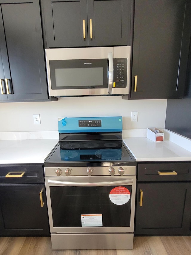 kitchen with light wood-type flooring, appliances with stainless steel finishes, light countertops, and dark cabinetry