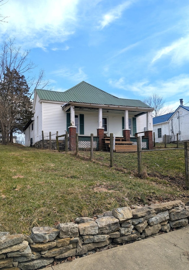 view of front of house featuring metal roof, a porch, a fenced front yard, and a front yard