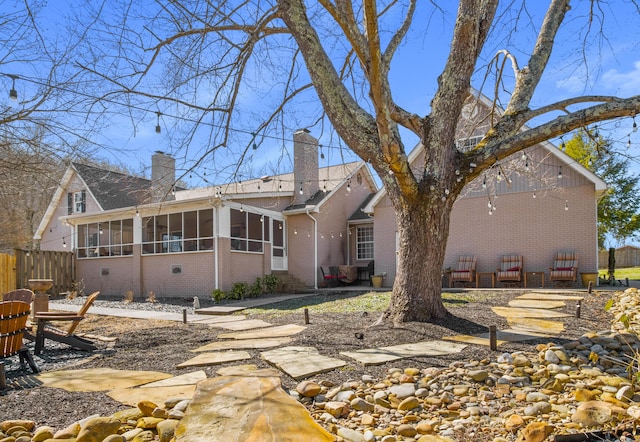 back of property with brick siding, a sunroom, fence, and a chimney