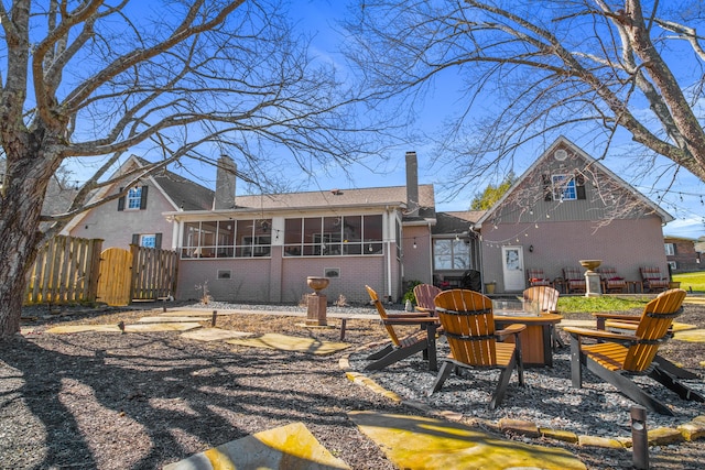 rear view of property with a sunroom, brick siding, an outdoor fire pit, a chimney, and fence