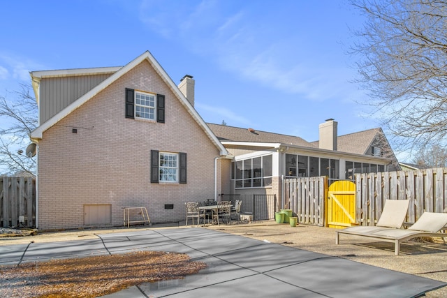 back of house with a sunroom, brick siding, a patio, a chimney, and fence
