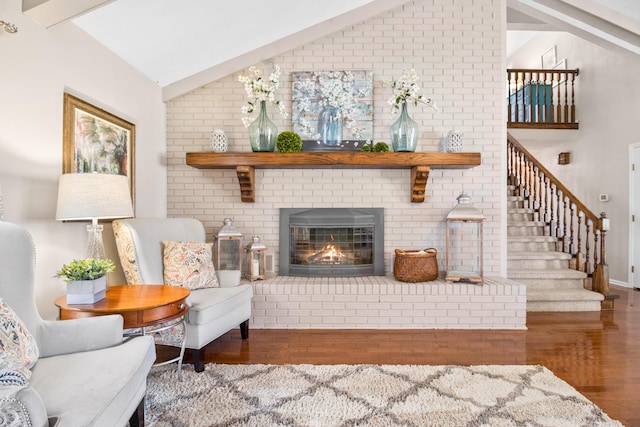 living area featuring lofted ceiling, wood finished floors, stairway, a brick fireplace, and baseboards