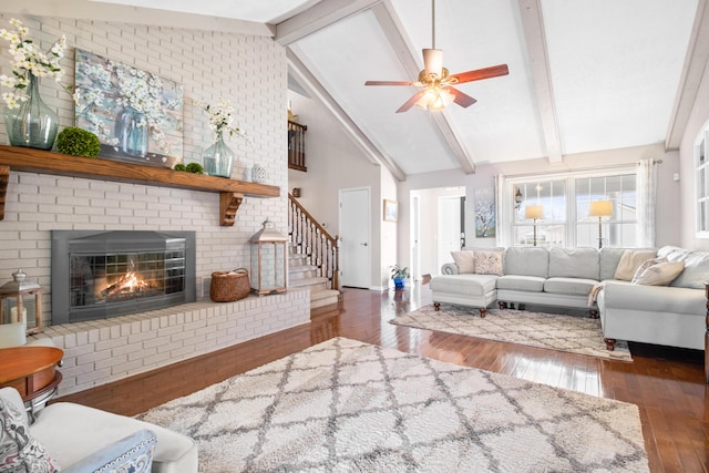 living area featuring hardwood / wood-style floors, a ceiling fan, beam ceiling, a fireplace, and stairway