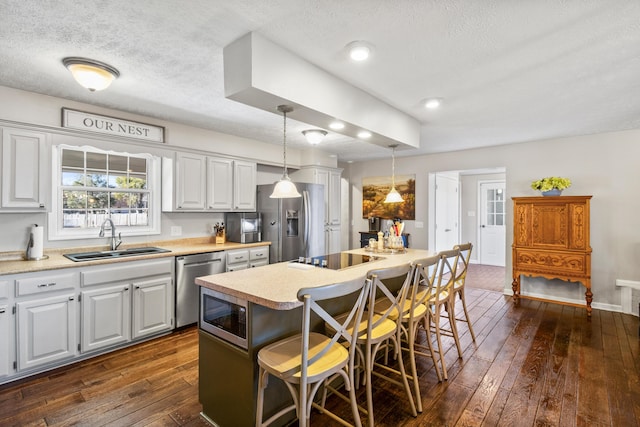 kitchen with a sink, appliances with stainless steel finishes, a kitchen island, dark wood-style flooring, and a textured ceiling