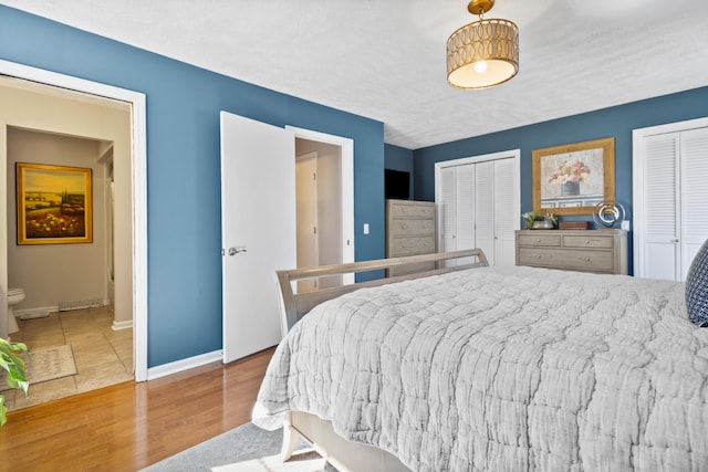 bedroom with multiple closets, wood finished floors, baseboards, and connected bathroom