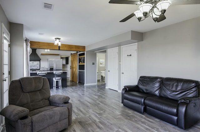 living area with visible vents, a barn door, a ceiling fan, wood finished floors, and baseboards