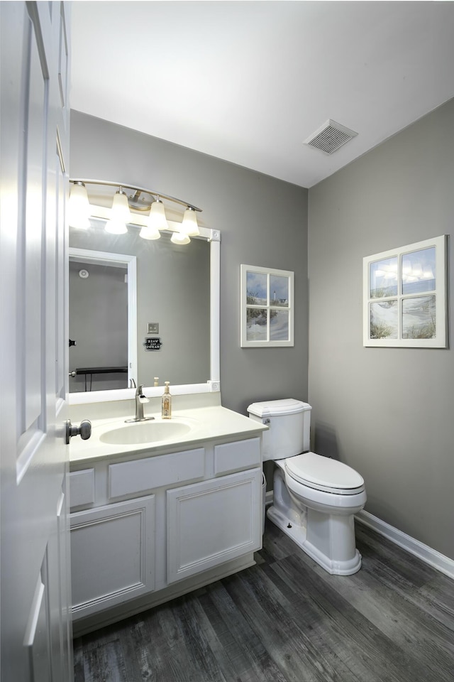 bathroom featuring baseboards, visible vents, toilet, wood finished floors, and vanity