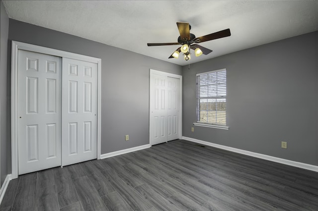 unfurnished bedroom with ceiling fan, a textured ceiling, dark wood-style flooring, baseboards, and multiple closets