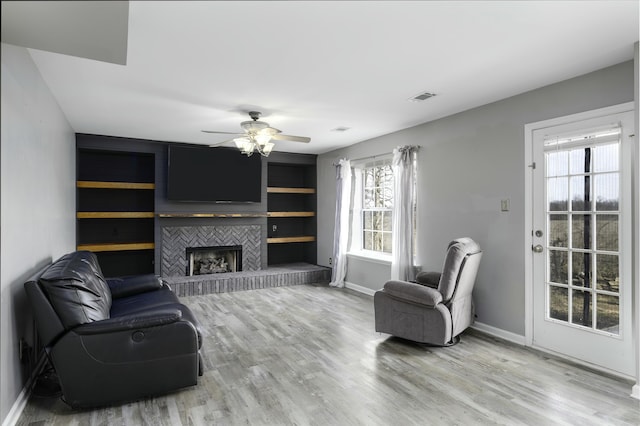 living room featuring visible vents, a ceiling fan, a brick fireplace, light wood-type flooring, and baseboards