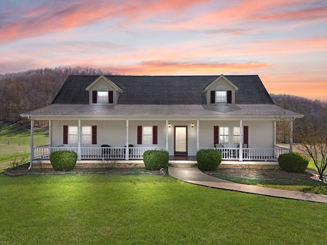 farmhouse with a shingled roof, a porch, and a lawn