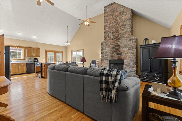 living room with ceiling fan, a textured ceiling, light wood-type flooring, a fireplace, and high vaulted ceiling