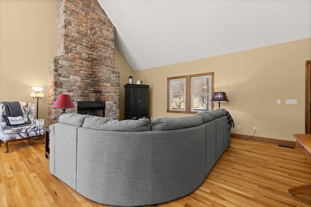 living room featuring light wood-type flooring, a fireplace, high vaulted ceiling, and baseboards