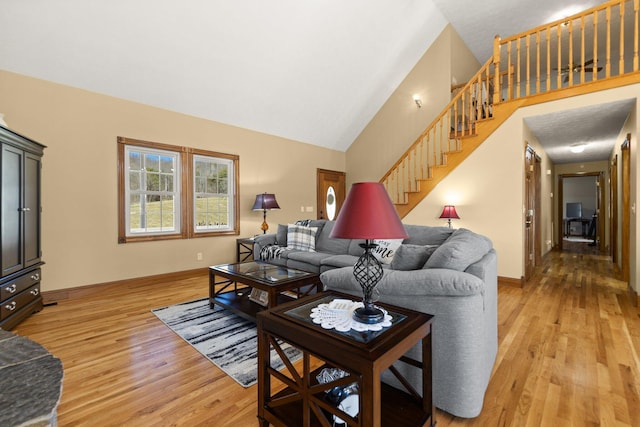 living room featuring high vaulted ceiling, stairway, light wood-style flooring, and baseboards