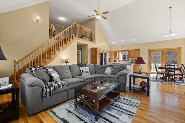 living area featuring light wood finished floors, stairway, high vaulted ceiling, and ceiling fan with notable chandelier